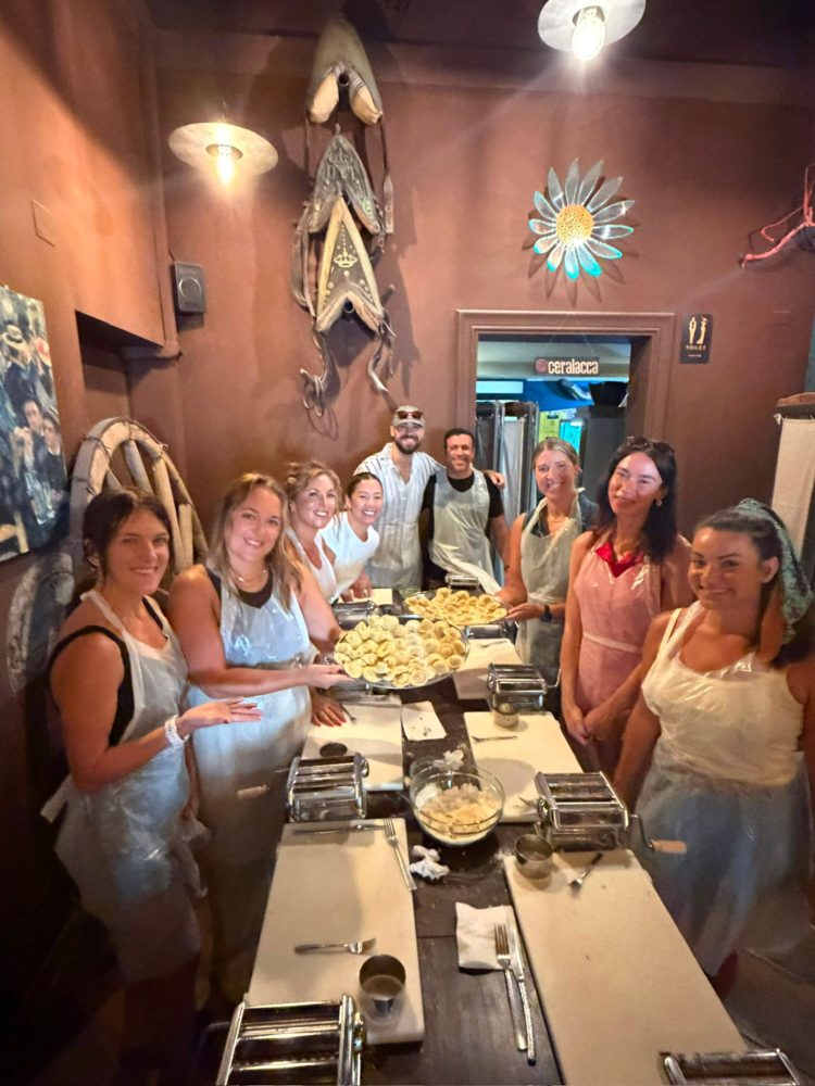 The crew in aprons holding trays of fresh pasta at a class in Bari