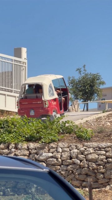 A red tuk-tuk on a hill road above a stone wall